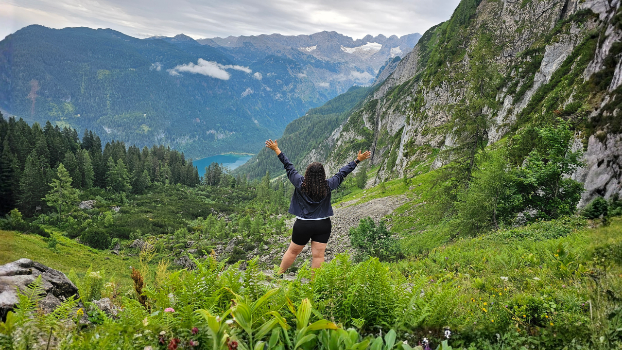Lucie McGuire standing with arms open on a mountainside overlooking a lake